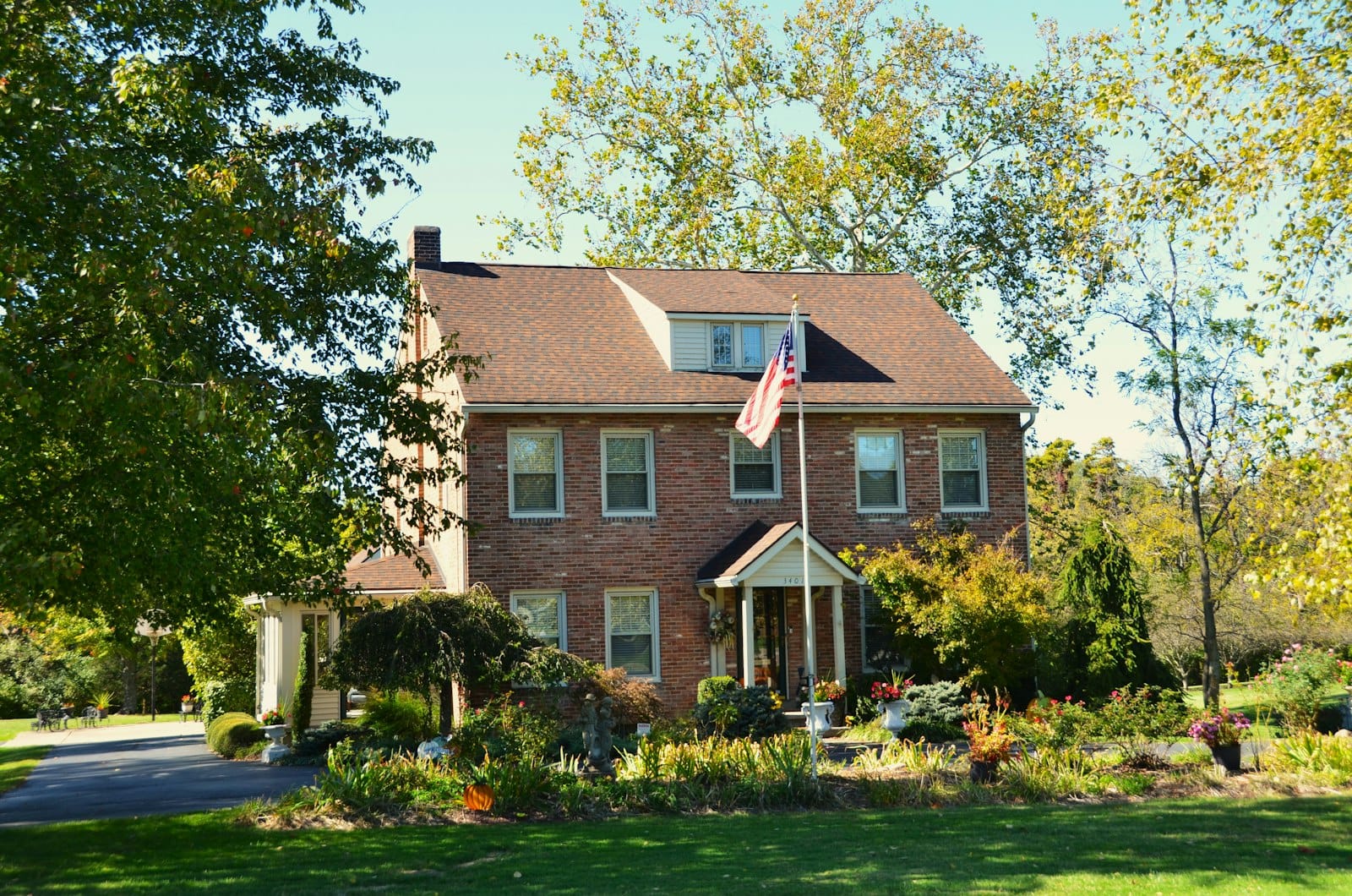 A brick colonial house with an American flag in the fall